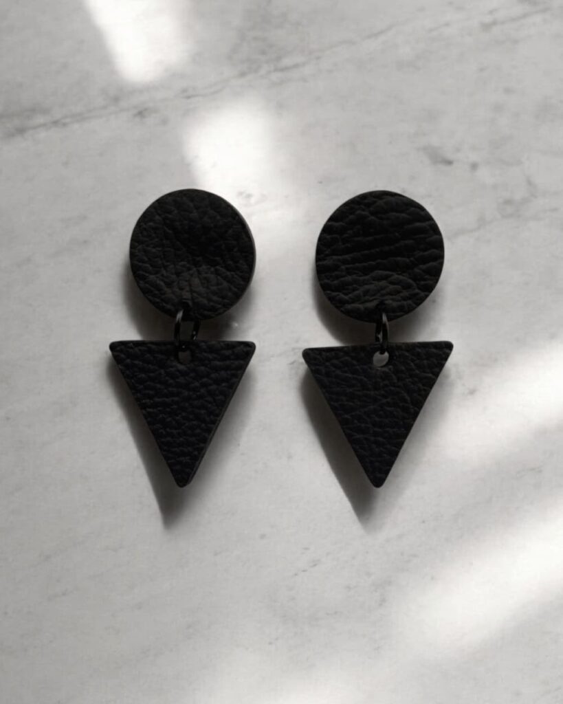 Schwarze Lederohrringe in runder und dreieckiger Form – handgefertigter Unisex-Lederschmuck von GEOTI auf hellem Hintergrund