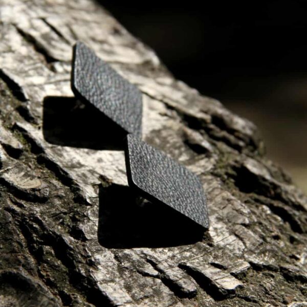 Schwarze Ohrringe aus Leder mit quadratischer Form, handgefertigt, auf Baumrinde fotografiert.
