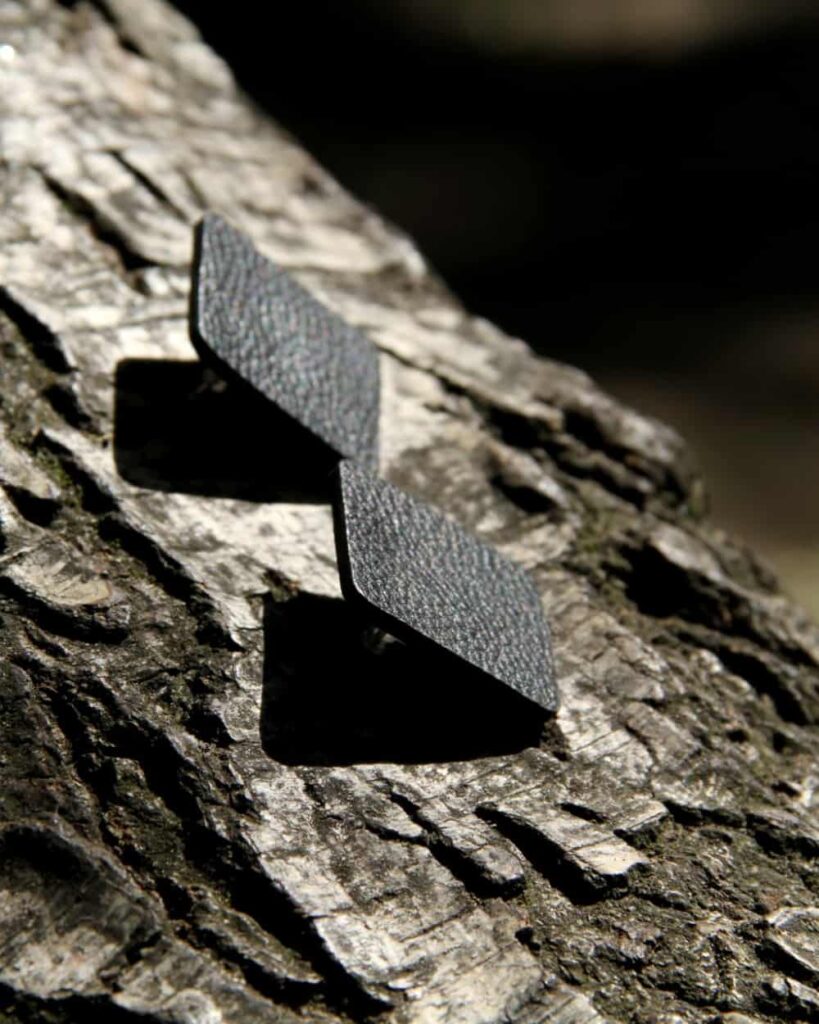 Schwarze Ohrringe aus Leder mit quadratischer Form, handgefertigt, auf Baumrinde fotografiert.