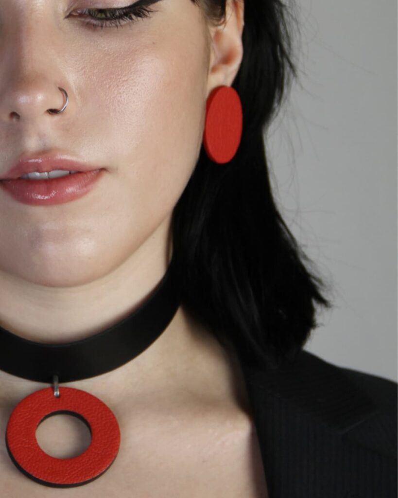 Nahaufnahme von handgefertigten Ohrringen und Choker aus rotem Leder mit Edelstahl, getragen von einer Frau